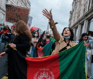 People protesting and holding the Afghanistan flag. Sign in back that reads "Stop Proxy War in Afghanistan"