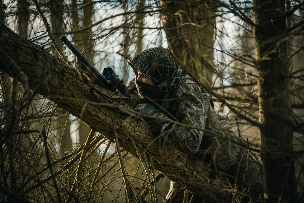 Person in camoflauge on a tree holding a gun