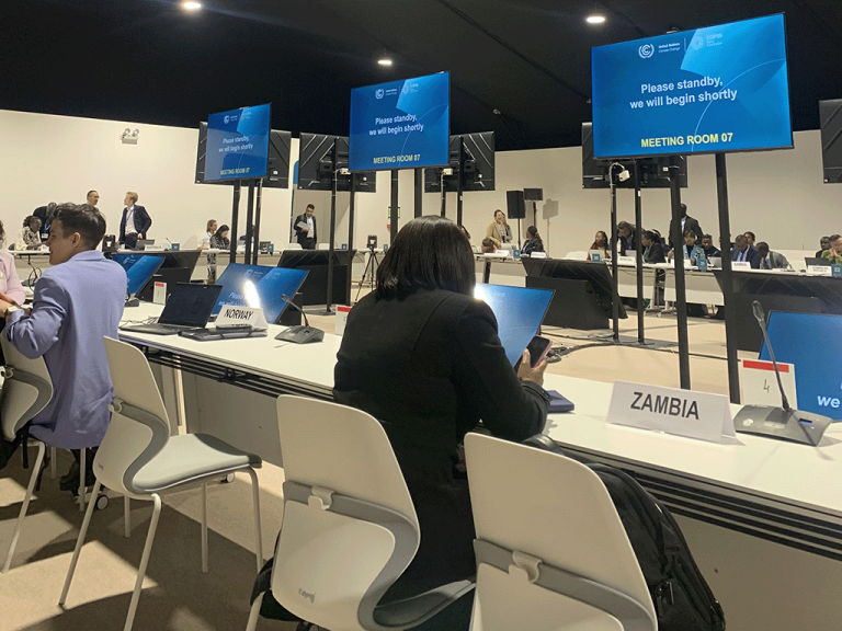 Negotiators prepare for a session at COP29, Baku. A woman sits at a desk, facing away from the camera, with a row of screens in front climate, climate crisis, loss and damage, climate finance, just transition