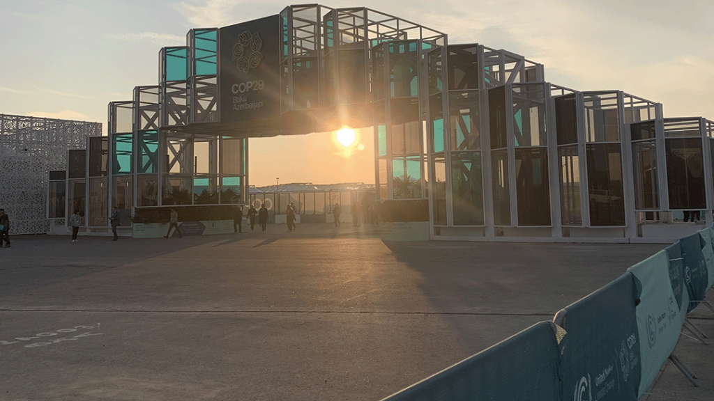 The sun sets behind a gateway bearing the logo for COP29, Baku Climate, climate justice, climate loss and damage