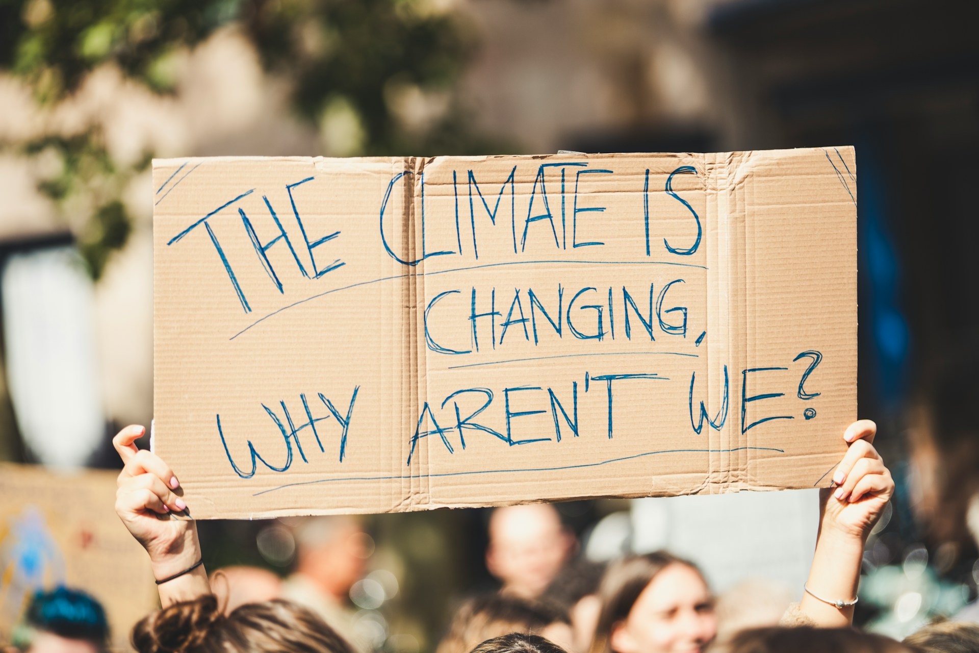 A person holding a cardboard sign saying" The climate is changing, why aren't we?" care work and the climate emergency